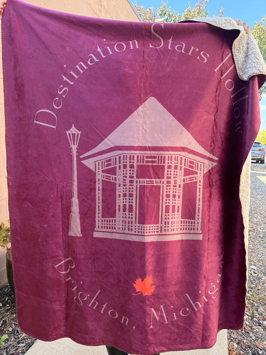 Maroon blanket with white text and design, draped over a surface outdoors.